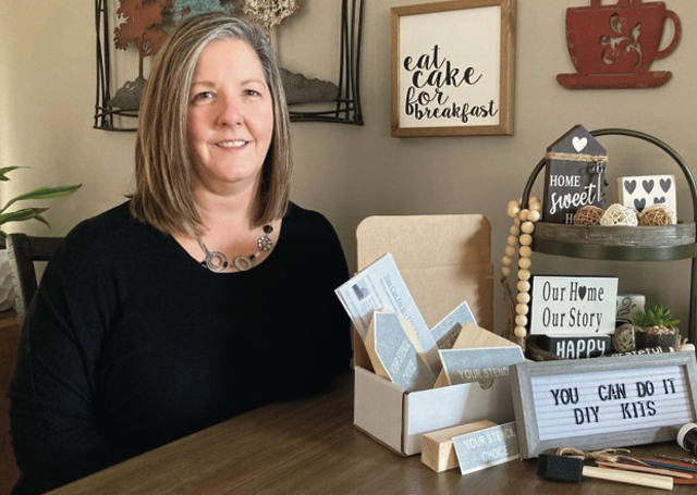 Lisa Miller of You Can Do It DIY Kits seated at a table with some of her wooden sign kits.